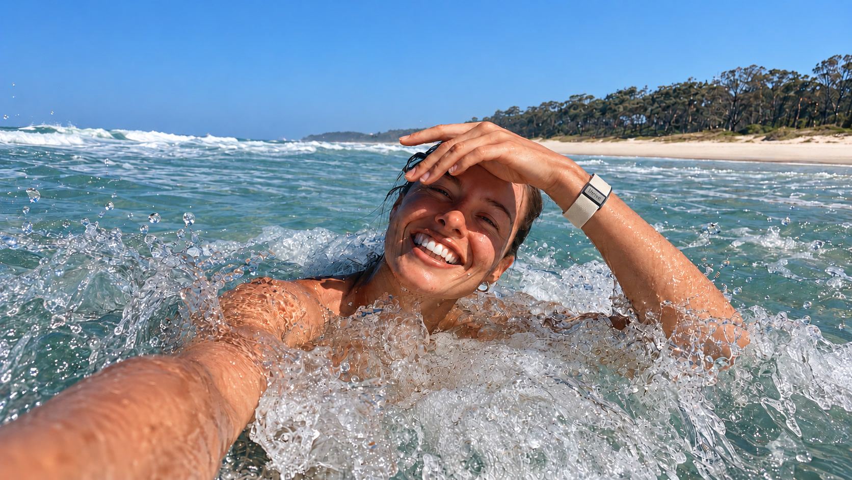 A woman laughing in the surf at an Australian beach, wearing the Thrive Health Band in Flat White